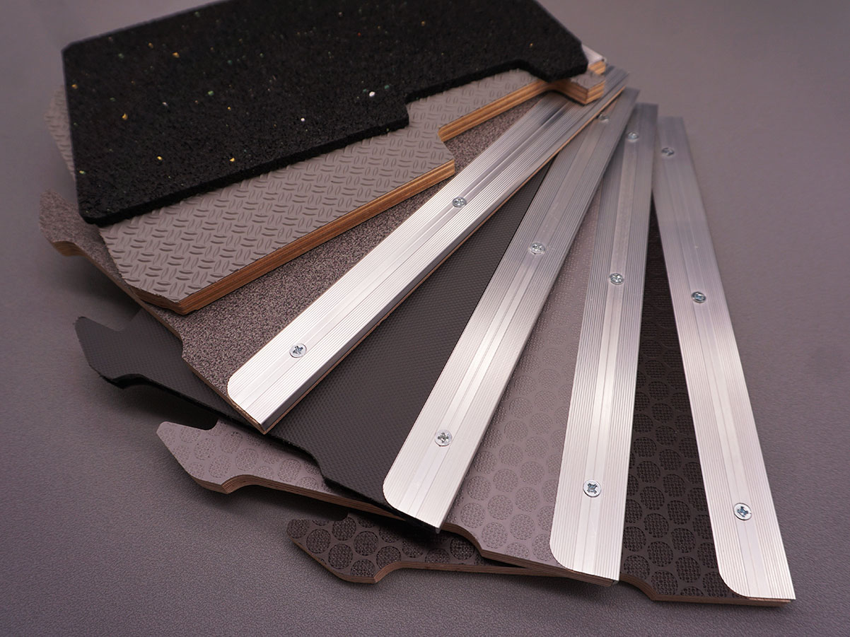 Mehrere geschichtete Trittschutzplatten aus Holz, Kunststoff und Aluminiumprofilen mit Schrauben, übereinander angeordnet.